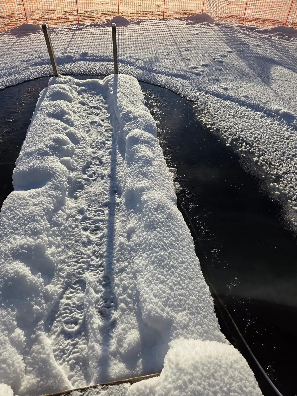 Höyryävä avanto ja lumiset portaat aurinkoisena pakkasaamuna